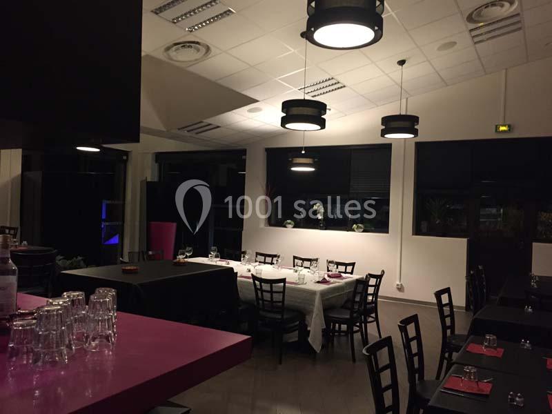 Salle de restaurant vide avec tables dressées, éclairage suspendu et ambiance tamisée.