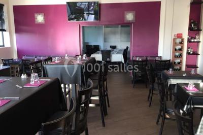 Terrasse en bois avec tables, chaises colorées et parasols verts et rouges, entourée de végétation et de bâtiments.