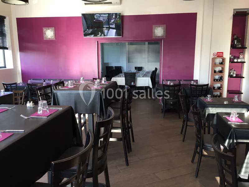 Salle de restaurant avec tables dressées, nappes noires, chaises en bois foncé et murs violets.