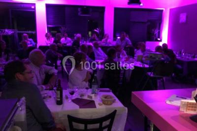 Terrasse en bois avec tables, chaises colorées et parasols verts et rouges, entourée de végétation et de bâtiments.