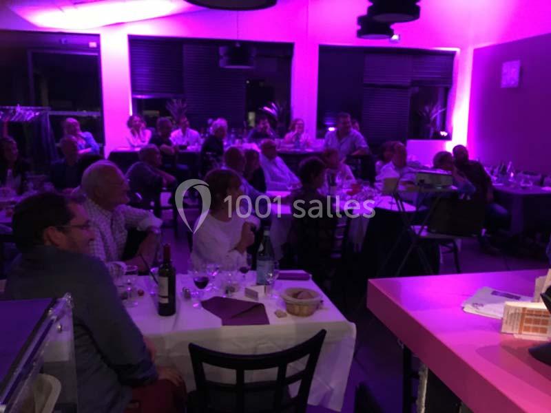 Des personnes assises à des tables dans une salle éclairée par des lumières violettes, participant à un événement.