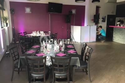 Terrasse en bois avec tables, chaises colorées et parasols verts et rouges, entourée de végétation et de bâtiments.