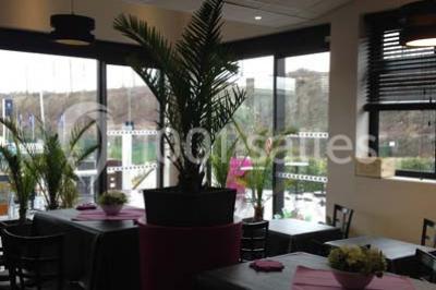 Terrasse en bois avec tables, chaises colorées et parasols verts et rouges, entourée de végétation et de bâtiments.