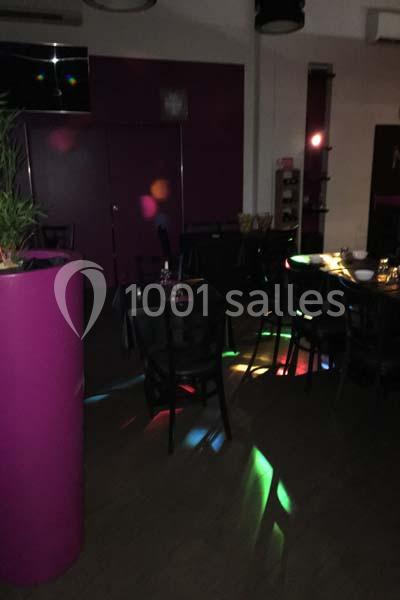 Salle sombre avec des tables et des chaises, éclairée par des lumières colorées projetées au sol.