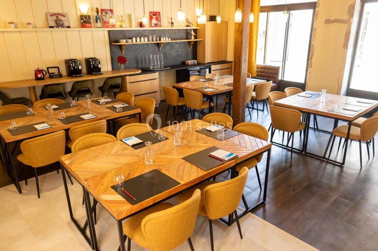 Salle de réunion lumineuse avec tables en bois, chaises jaunes, blocs-notes et carafes d'eau disposés.