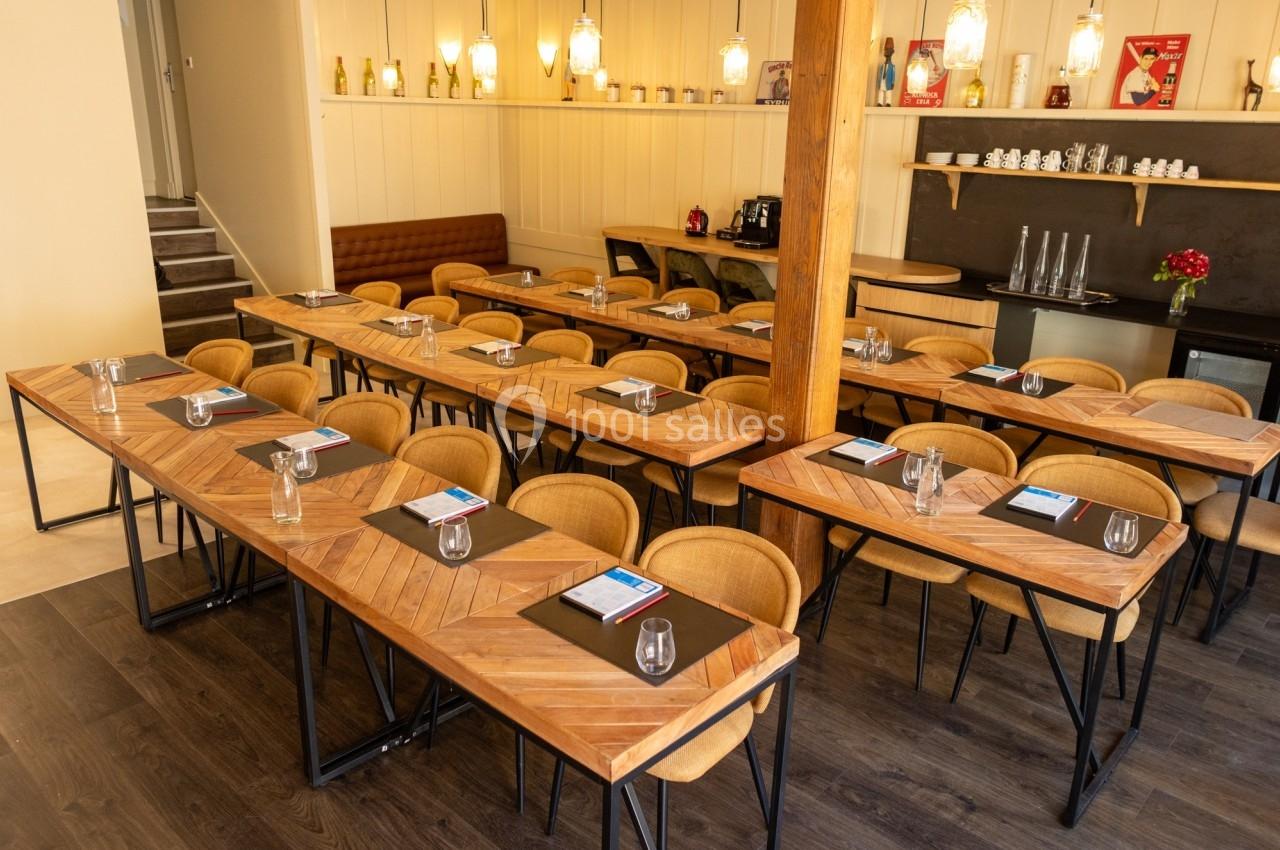 Salle aménagée avec des tables en bois disposées en rangées, chaises, verres et documents posés pour une réunion ou…