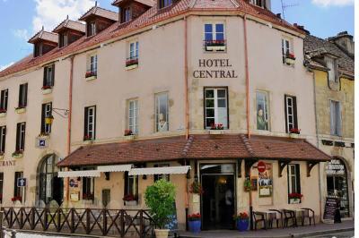 Petit-déjeuner avec croissant, jus d'orange et café sur un plateau, posé sur une table en bois près d'un vase de fleurs.