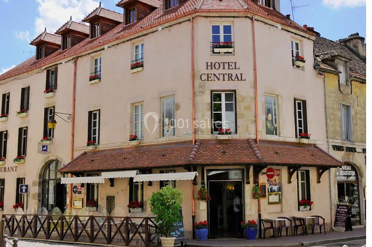 Façade d'un hôtel de style traditionnel avec des volets blancs, des fleurs aux fenêtres et une terrasse extérieure.