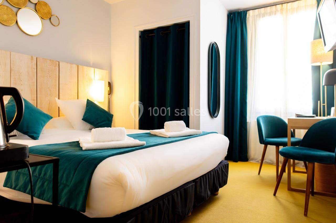 Chambre lumineuse avec lit double, draps blancs, coussins verts, bureau, chaises et rideaux assortis.