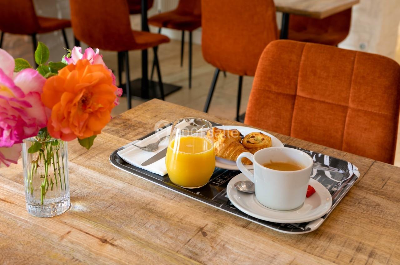 Petit-déjeuner avec croissant, jus d'orange et café sur un plateau, posé sur une table en bois près d'un vase de fleurs.