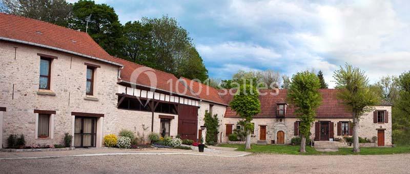 Bâtisse en pierre avec toits en tuiles rouges, entourée de végétation et située dans une cour gravillonnée.