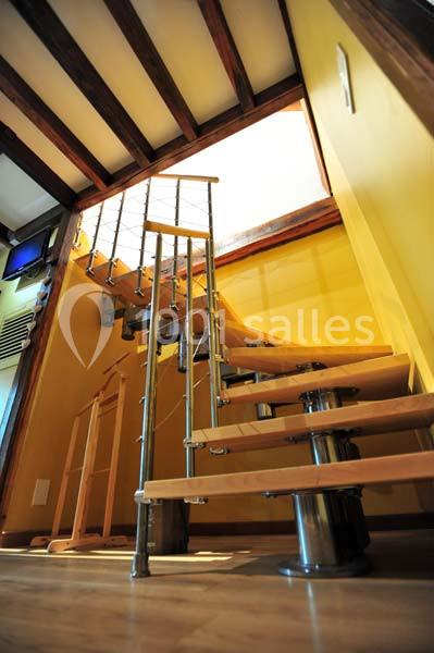 Escalier en bois et métal avec des marches suspendues, situé dans un intérieur aux murs jaunes et plafond en poutres…