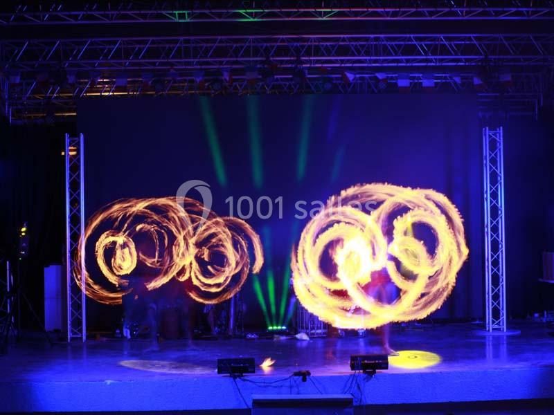 Des artistes réalisent une performance de jonglage lumineux avec des cercles de feu sur une scène éclairée.