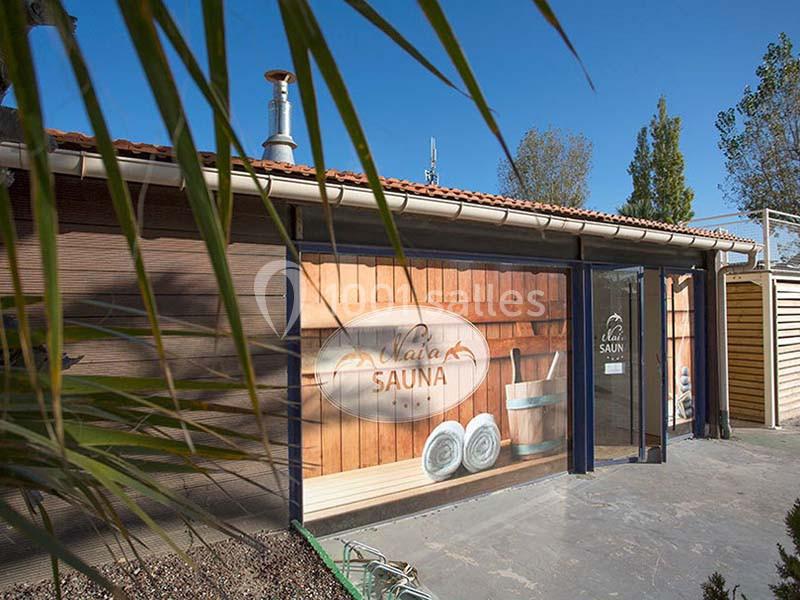 Façade d'un bâtiment avec une enseigne ’Sauna’, entourée de végétation et éclairée par la lumière du jour.
