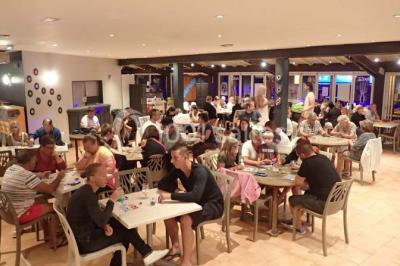 Groupe de personnes assises à des tables en extérieur, assistant à un spectacle sur une scène éclairée en soirée.