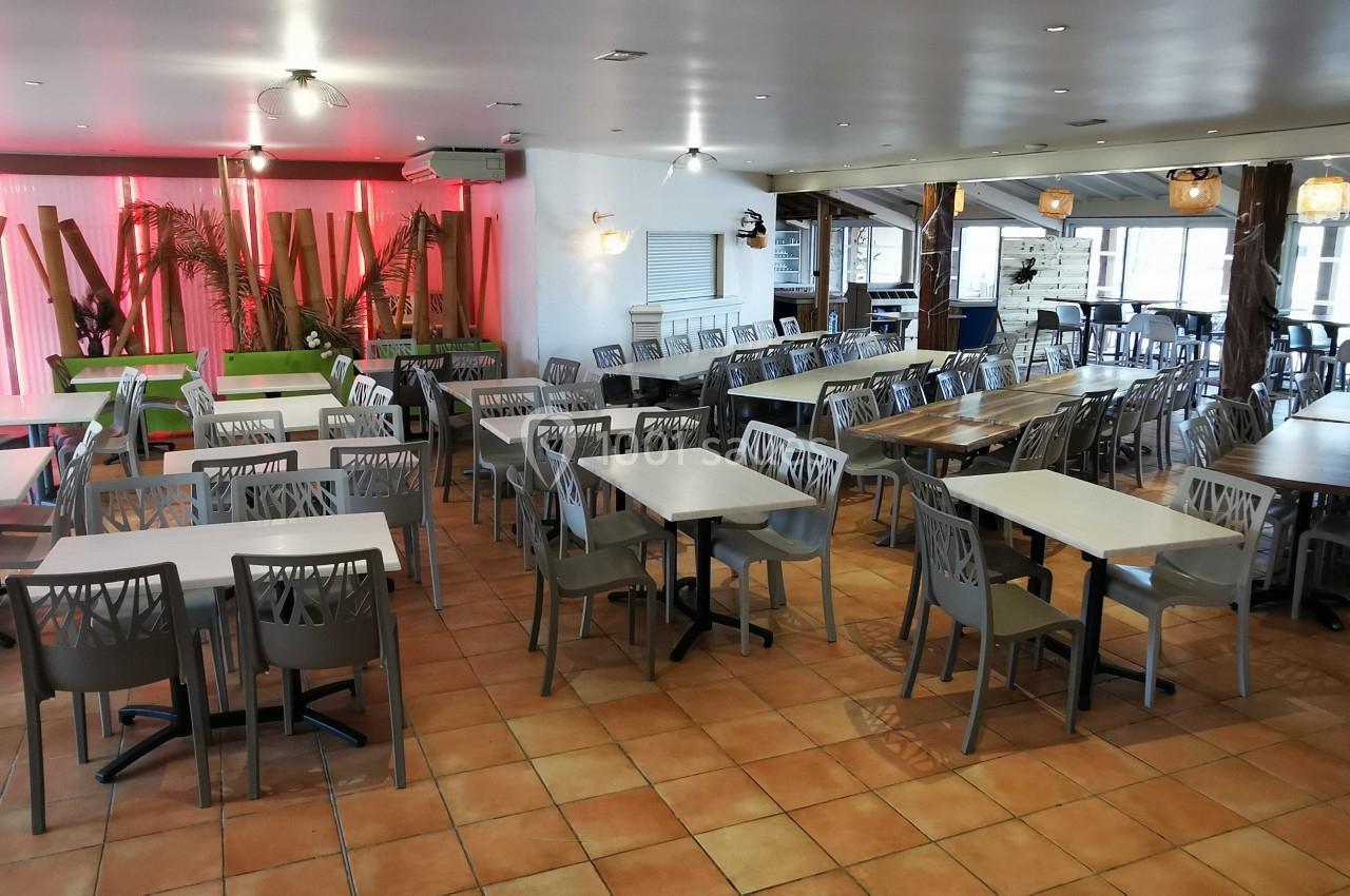 Salle de restaurant spacieuse avec des tables et chaises alignées sur un sol en carrelage, éclairée par des lumières…