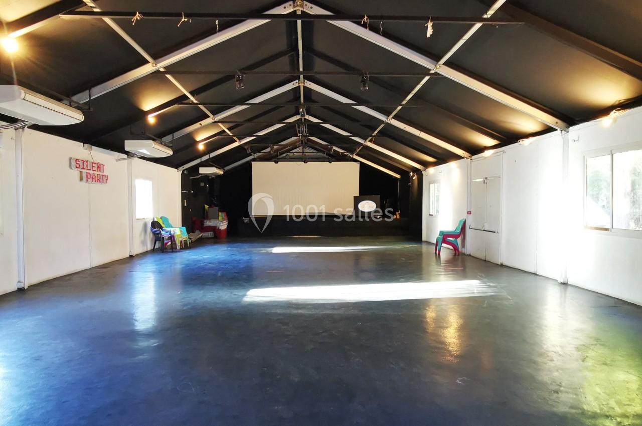 Salle vide avec un sol sombre, des murs blancs, un plafond noir incliné et une scène au fond.