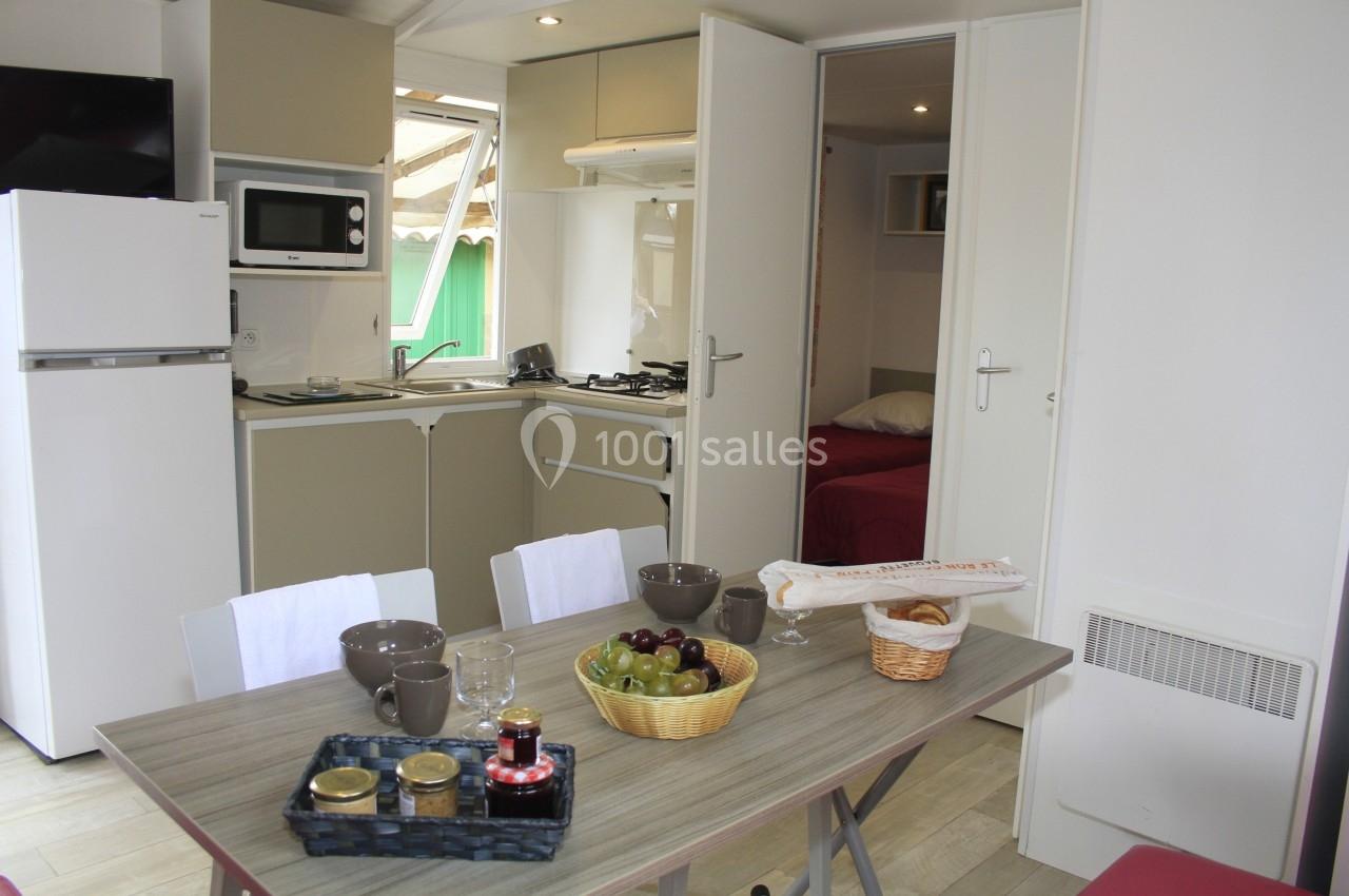 Cuisine ouverte avec table dressée, réfrigérateur, micro-ondes, et vue sur une chambre à travers des portes ouvertes.