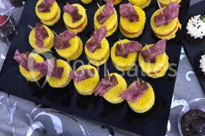 Cuillères transparentes disposées en cercle sur une assiette noire, remplies de semoule garnie de légumes et herbes.