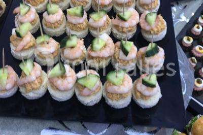 Cuillères transparentes disposées en cercle sur une assiette noire, remplies de semoule garnie de légumes et herbes.