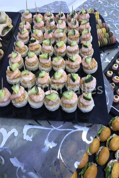 Plateau de canapés garnis de crevettes, concombres et sauce, disposés sur une nappe à motifs.