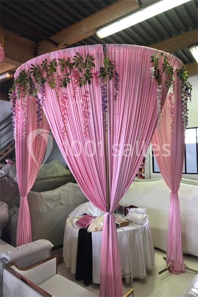 Structure décorative circulaire en tissu rose drapé, ornée de guirlandes florales suspendues, dans un espace intérieur.