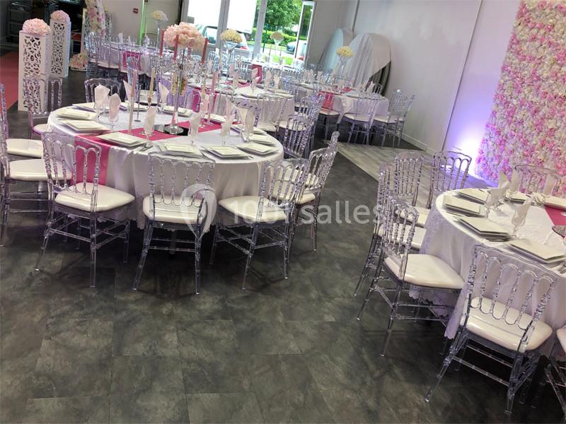 Salle de réception décorée avec des tables rondes dressées, chaises transparentes et murs ornés de fleurs.