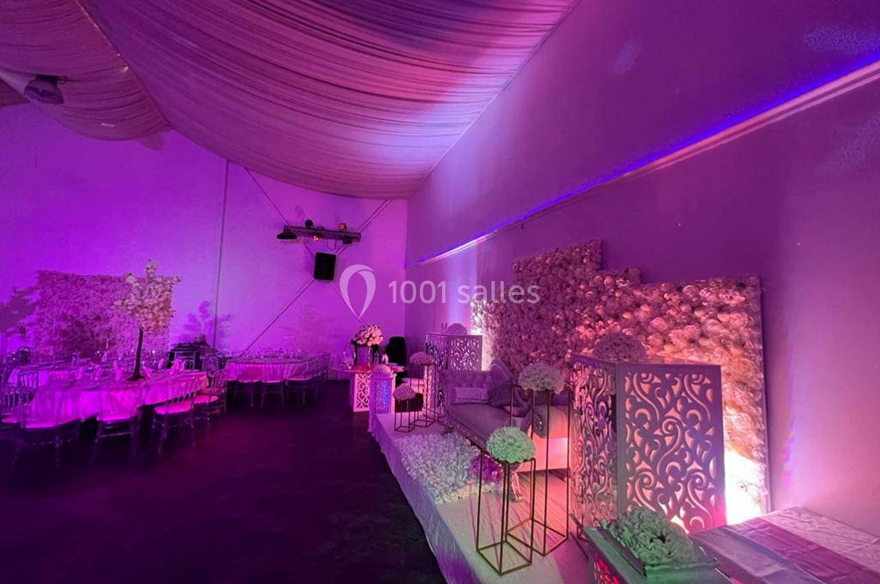 Salle de réception décorée avec des fleurs, des tables dressées et un éclairage violet tamisé.