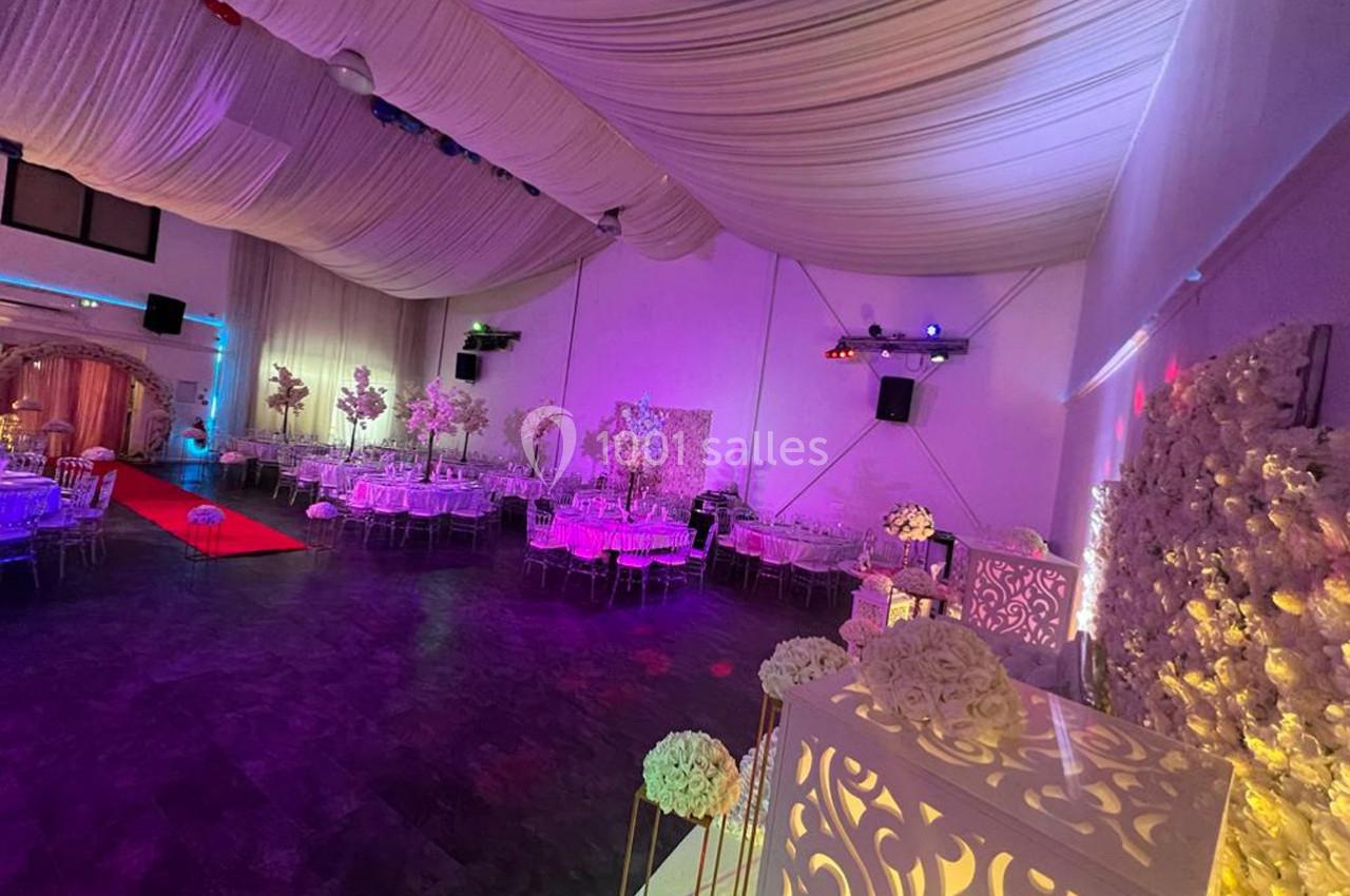 Salle de réception décorée avec des tables dressées, éclairage coloré et plafond drapé.