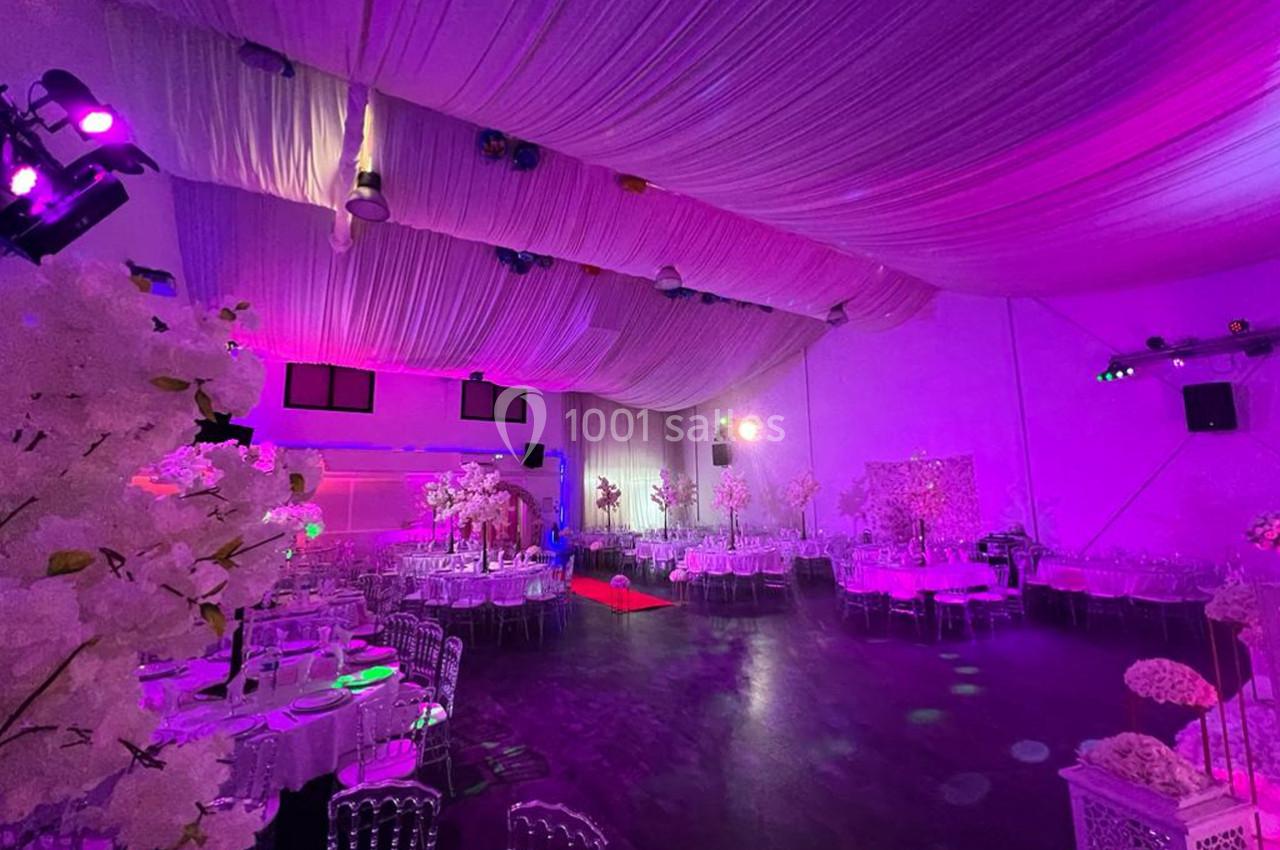 Salle de réception décorée avec des tables rondes, des chaises transparentes et un éclairage rose-violet.