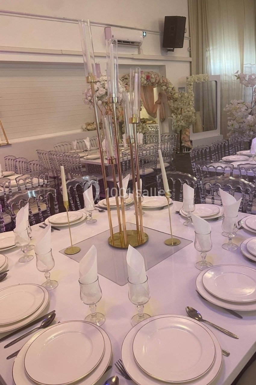 Table élégamment dressée avec vaisselle blanche, serviettes pliées et centre de table décoratif dans une salle ornée de…