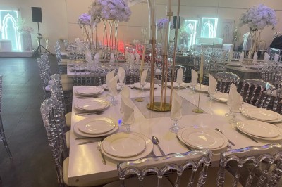 Allée centrale décorée de fleurs blanches et roses, avec arche florale et tables dressées pour un événement festif.