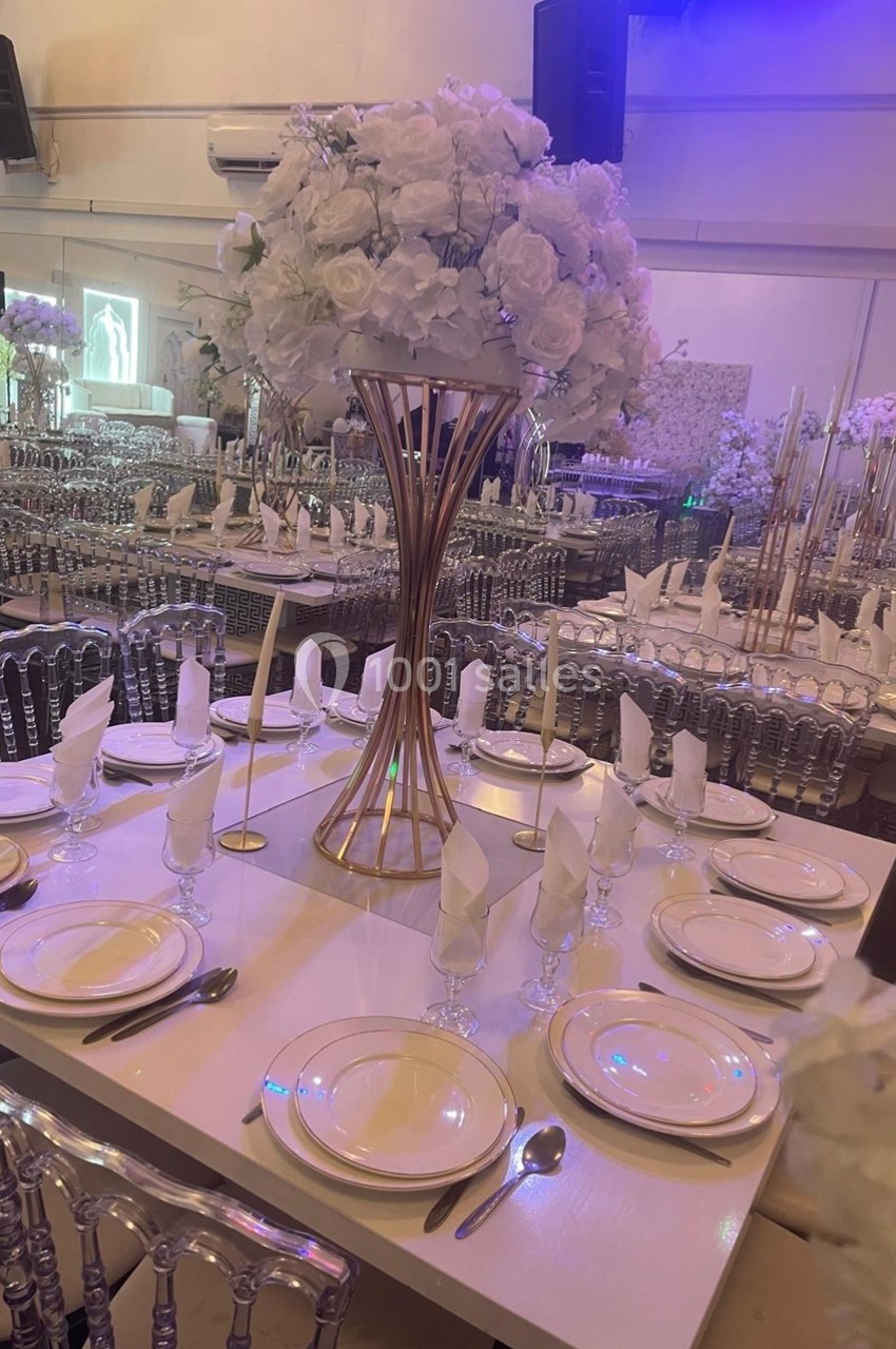 Salle de réception décorée avec des tables dressées, des chaises transparentes et un centre de table floral blanc élégant.