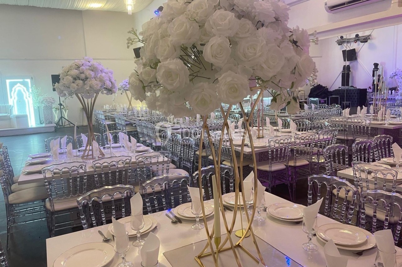 Salle de réception décorée avec des tables dressées, des chaises transparentes et des centres de table composés de roses…