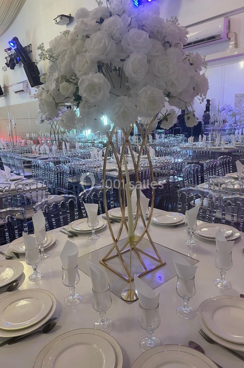 Centre de table avec des fleurs blanches sur une table dressée avec vaisselle et verres dans une salle de réception élégante.