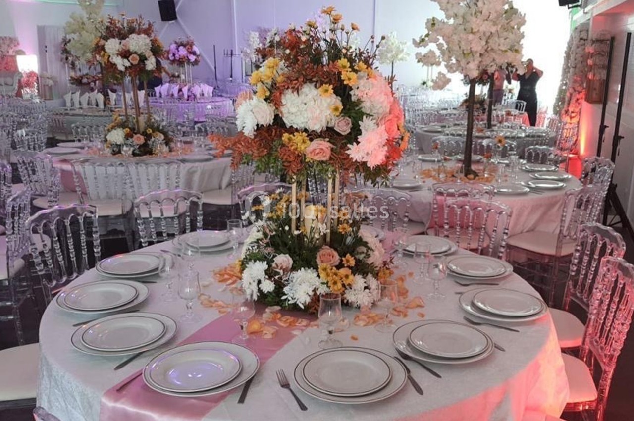 Table ronde décorée pour un événement, avec nappes blanches, vaisselle élégante et centre de table floral coloré.