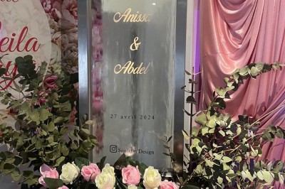 Allée centrale décorée de fleurs blanches et roses, avec arche florale et tables dressées pour un événement festif.