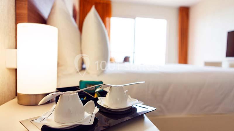 Deux tasses blanches avec cuillères sur un plateau, posées sur une table près d'une lampe dans une chambre lumineuse.