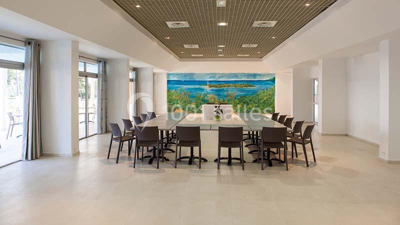 Salle de réunion lumineuse avec une grande table rectangulaire entourée de chaises et une fresque murale colorée.