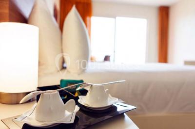 Deux tasses blanches avec cuillères sur un plateau, posées sur une table près d'une lampe dans une chambre lumineuse.