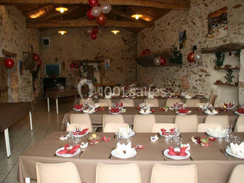 Salle de réception rustique décorée avec des ballons et des tables dressées pour un repas festif.