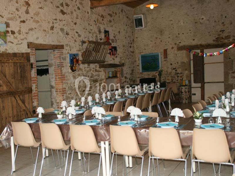 Salle de réception rustique avec murs en pierre, tables dressées avec nappes brunes, assiettes bleues et décorations…