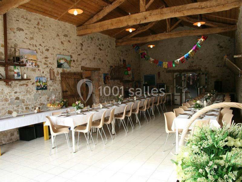 Salle de réception rustique avec tables dressées, chaises alignées et décoration festive suspendue.