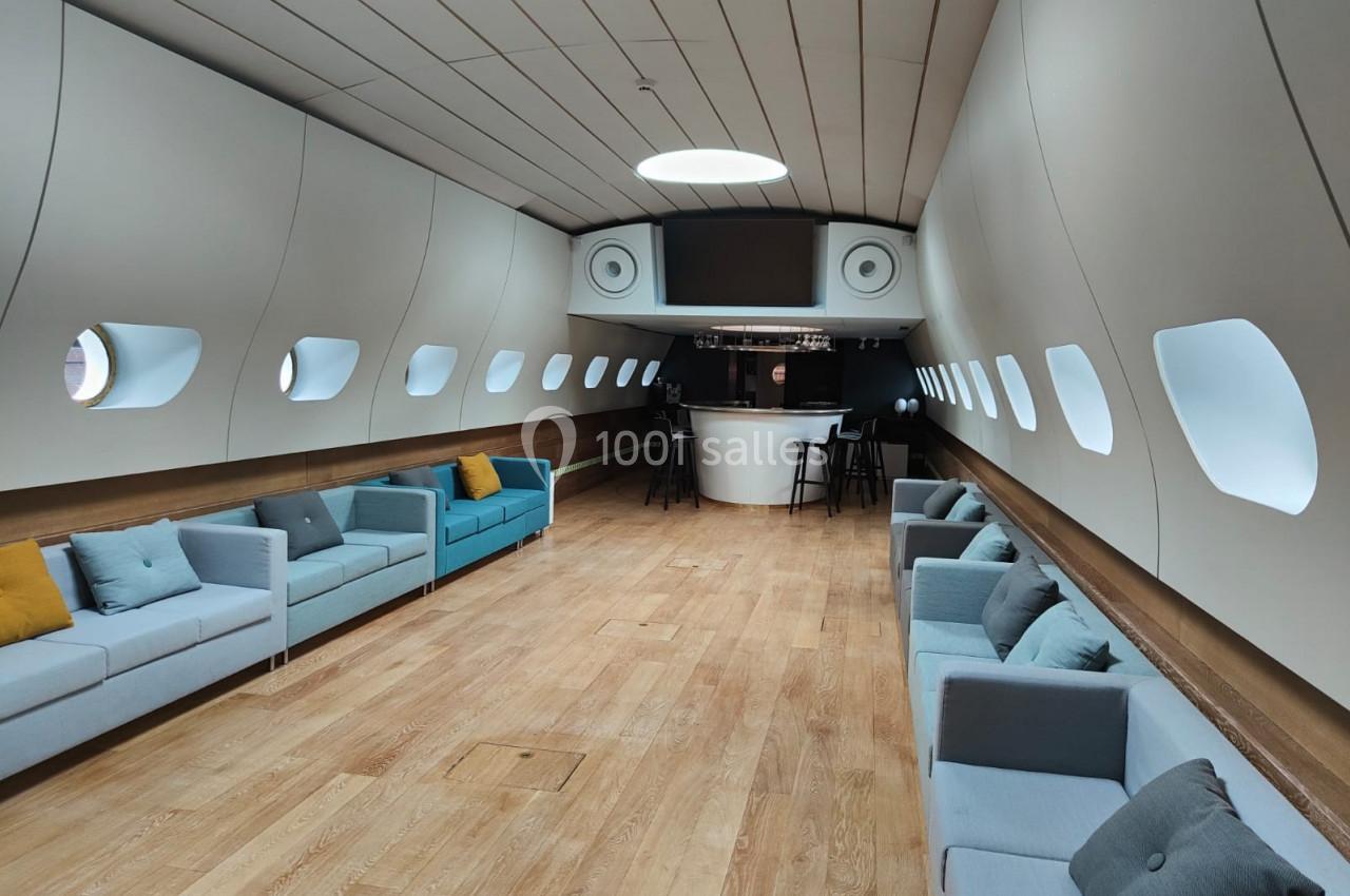 Intérieur spacieux d'un avion aménagé en salon avec canapés, parquet et un bar au fond.
