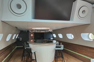 Cuisine étroite avec plaques de cuisson, étagères remplies de cartons et vaisselle, et un réfrigérateur en acier inoxydable.