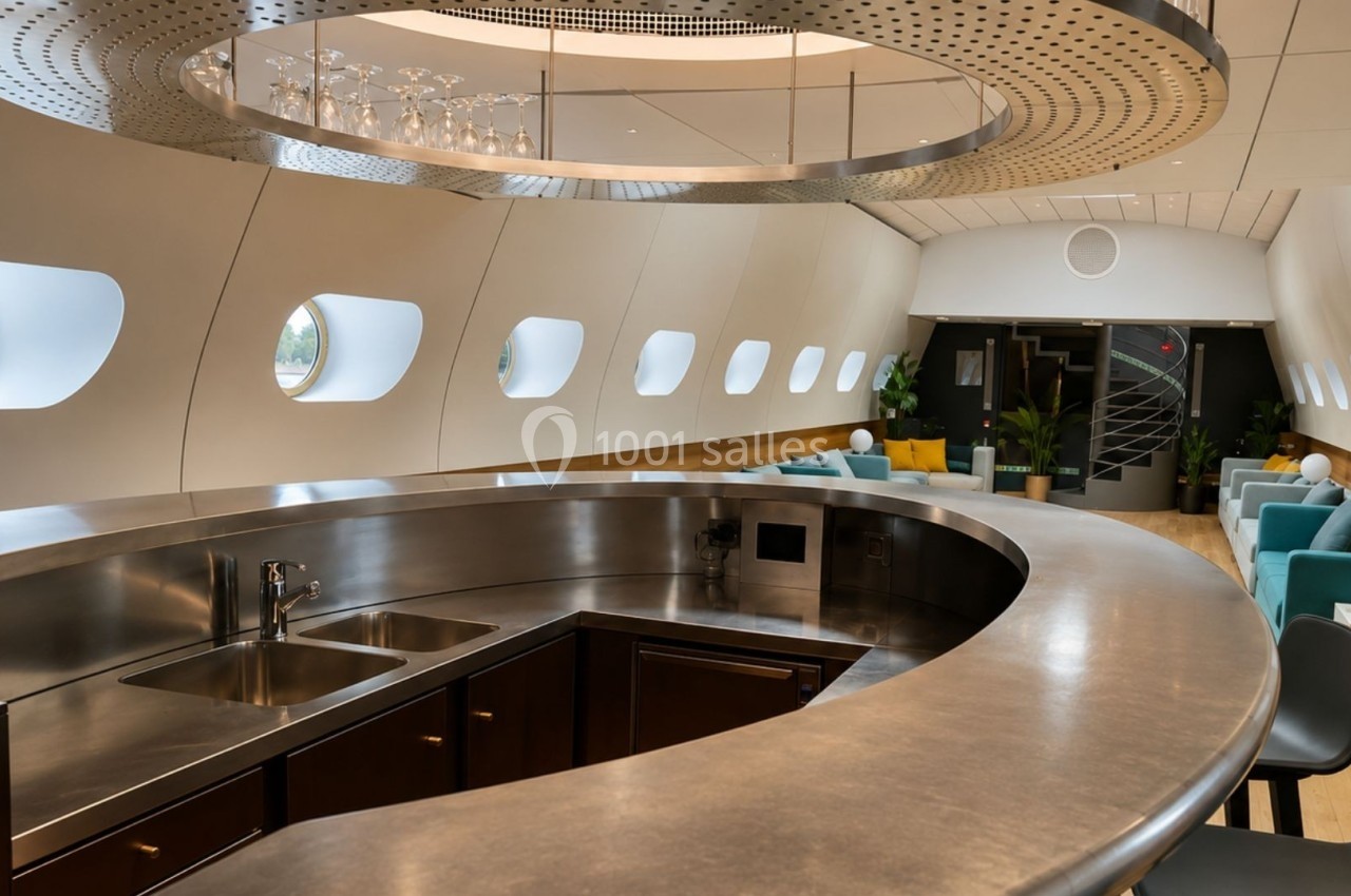 Intérieur moderne d'un espace aménagé avec un bar incurvé, des sièges confortables et des hublots ovales.