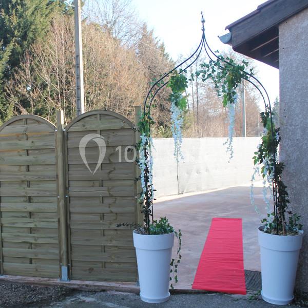 Arche décorée de feuillage et fleurs blanches, encadrée par deux pots blancs, avec un tapis rouge menant à une entrée…