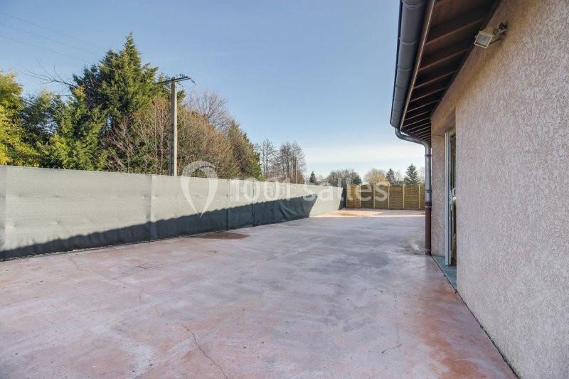 Cour extérieure en béton entourée de clôtures, avec un bâtiment à droite et des arbres en arrière-plan.