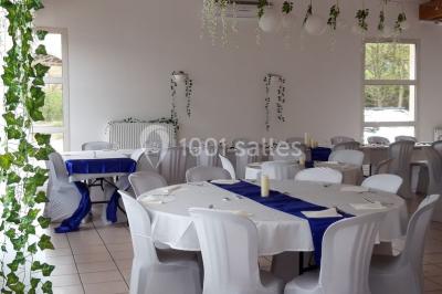 Salle lumineuse avec tables décorées de nappes blanches et chemins de table verts, prête pour un événement.