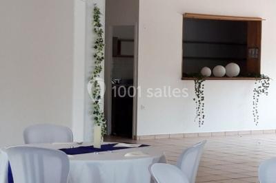 Salle lumineuse avec tables décorées de nappes blanches et chemins de table verts, prête pour un événement.